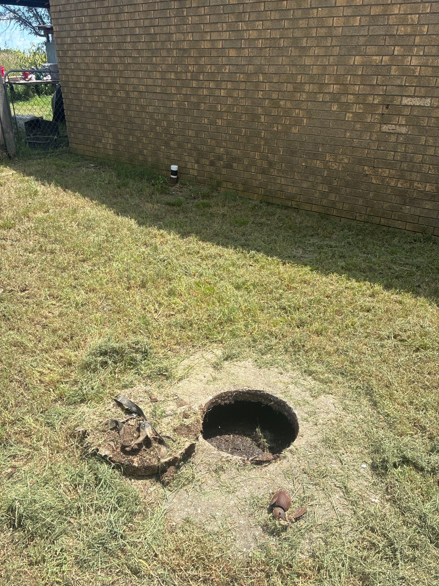 A failed septic tank with a collapsed lid and open hole in a yard